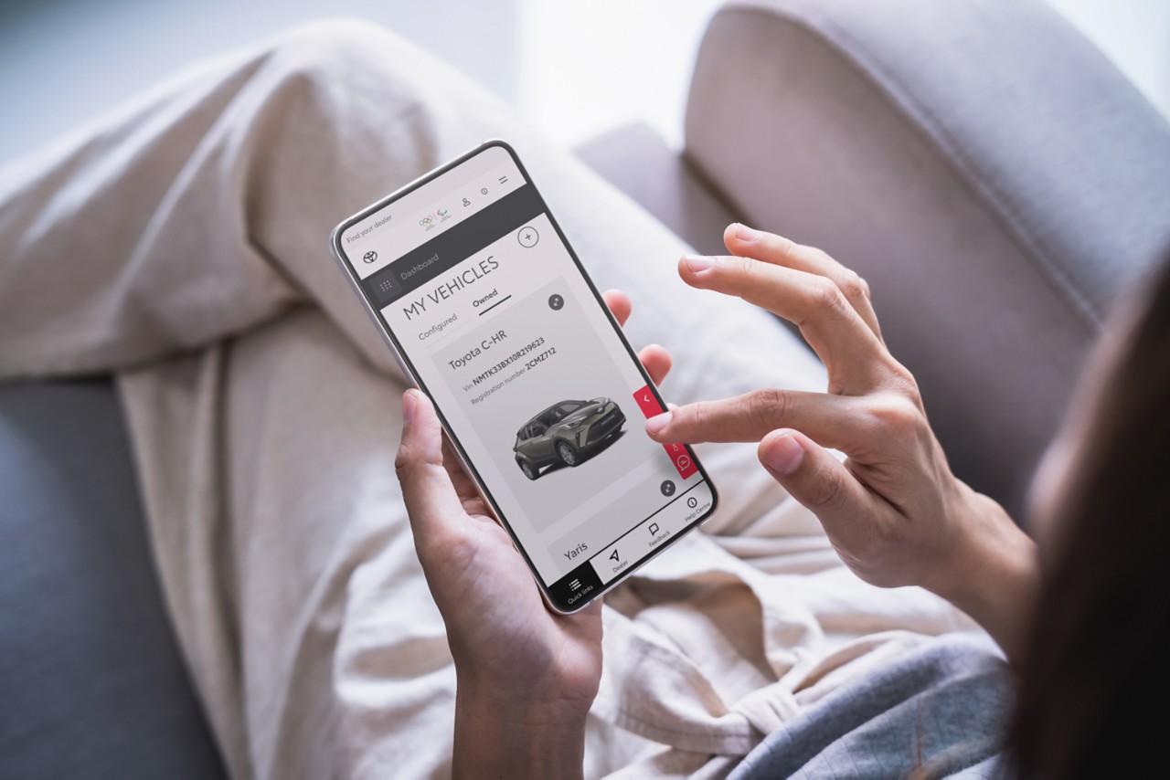 A woman taps the screen of her smartphone. It shows a Toyota C-HR on the My Vehicles page of the Toyota Personal Site.